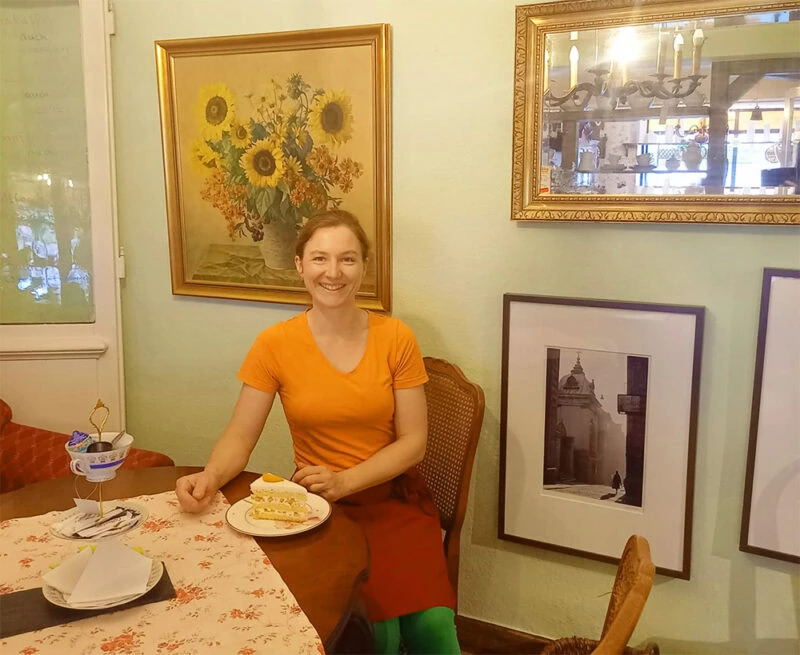 Sonniges Café-Anno-Dazumal mit freundlicher Kellnerin, gemütliche Atmosphäre, Kunst an den Wänden, perfekt für Kaffee und Kuchen.